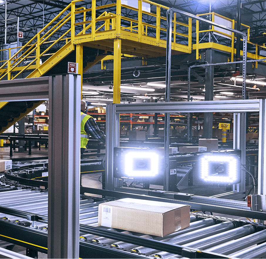 Close-up of a warehouse interior with a package on a roller conveyor in the foreground.