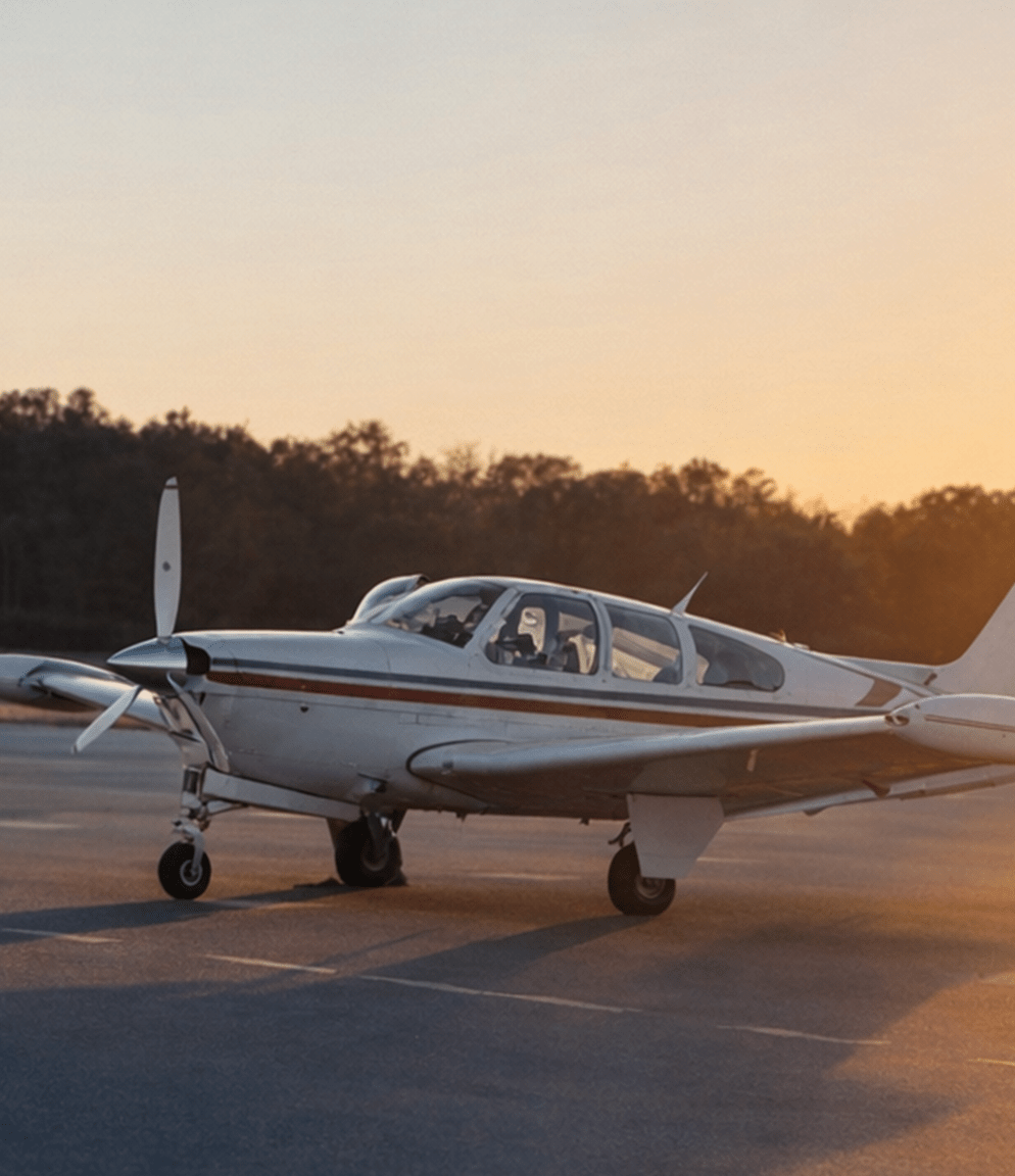 A single prop airplane sits on the tarmac, silhouetted against a sunrise.
